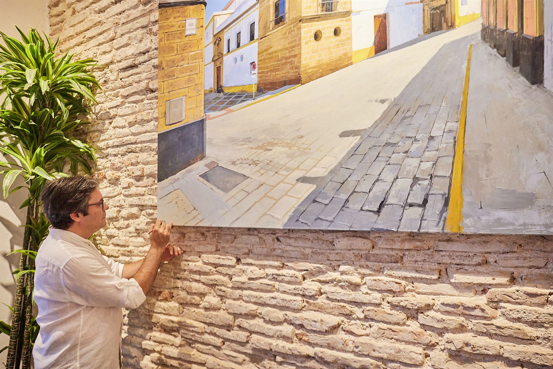 Muro de piedra ostionera y ladrillo visto de Donde Mané con un gran cuadro de una calle de Cádiz, mientras el pintor remata la obra.